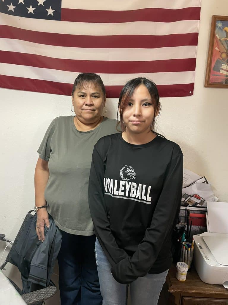 Two indigenous women stand in front of an American flag for a story marking the 5 year COVID anniversary