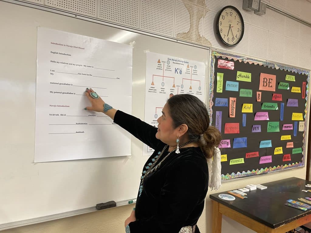 Lavinia Cody, an indigenous woman, gestures toward a poster on the wall for a story about the five year COVID anniversary